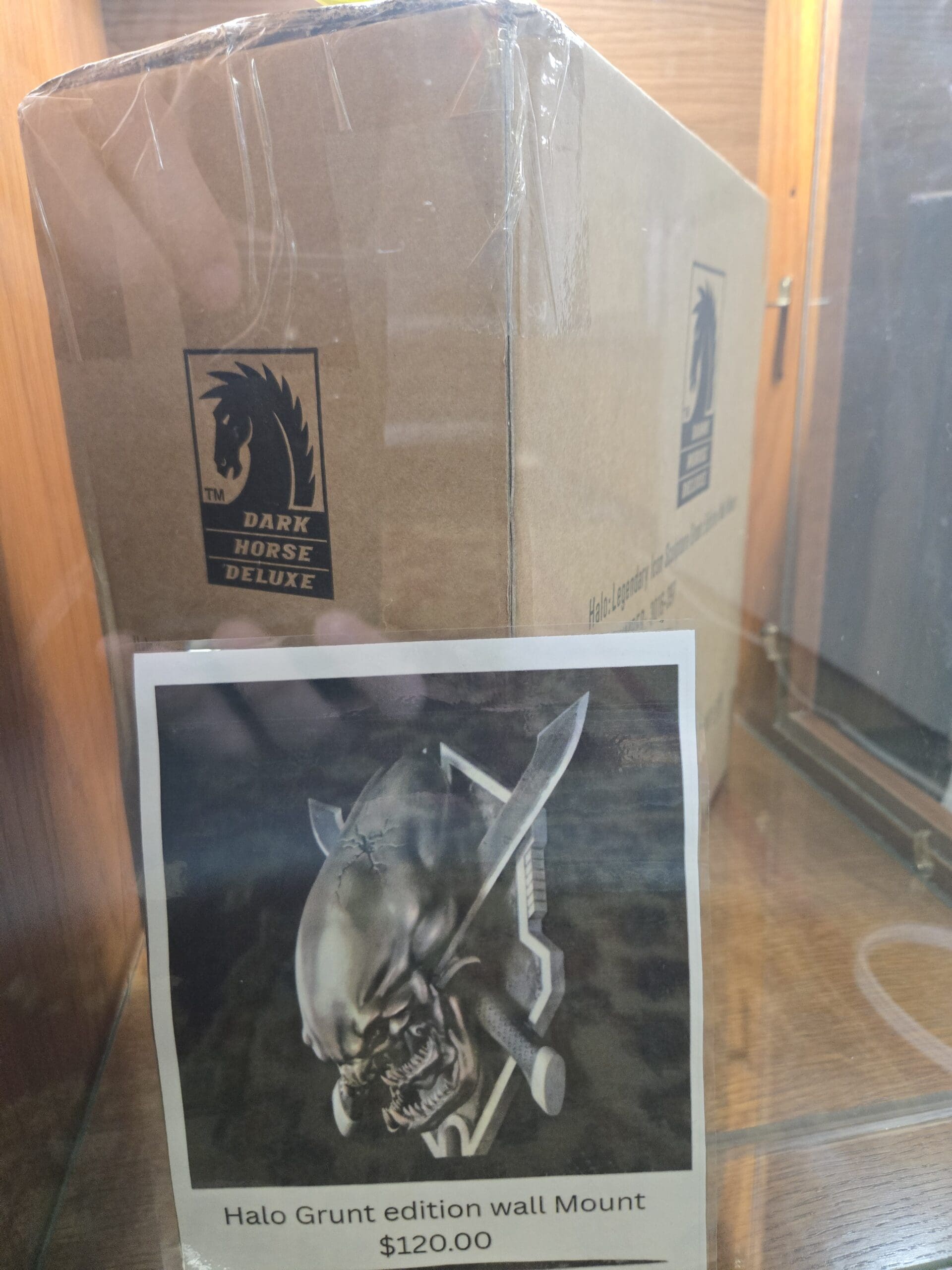 A factory-sealed Dark Horse Deluxe shipping box with a printed reference photo taped to the front showing a Halo Grunt edition wall mount, a sculpted Grunt head paired with a combat knife, on a wood shelf at Shop 117, Pacific Antiques Mall in Tacoma, WA.