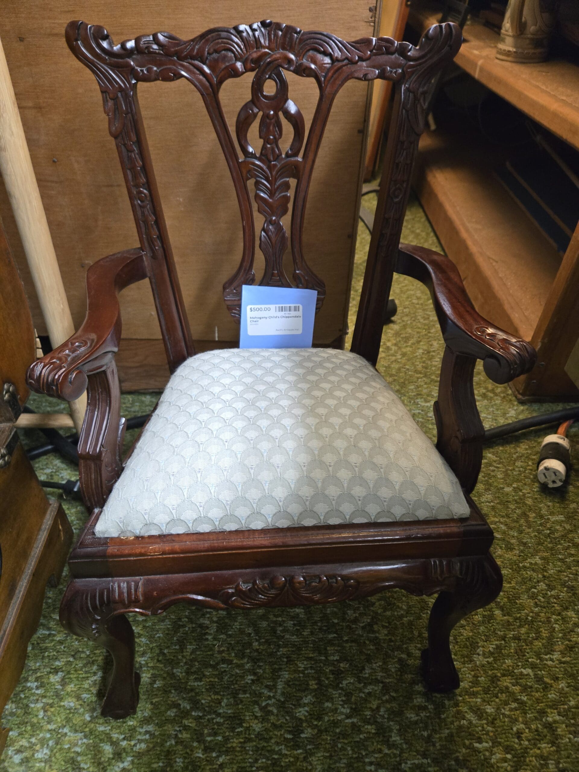 Mahogany child-sized Chippendale armchair with a carved pierced back splat, acanthus carved crest rail and arms, shell carved apron, ball and claw feet, and a drop-in seat upholstered in gray fan-pattern fabric at Shop 24, Pacific Antiques Mall in Tacoma, WA.