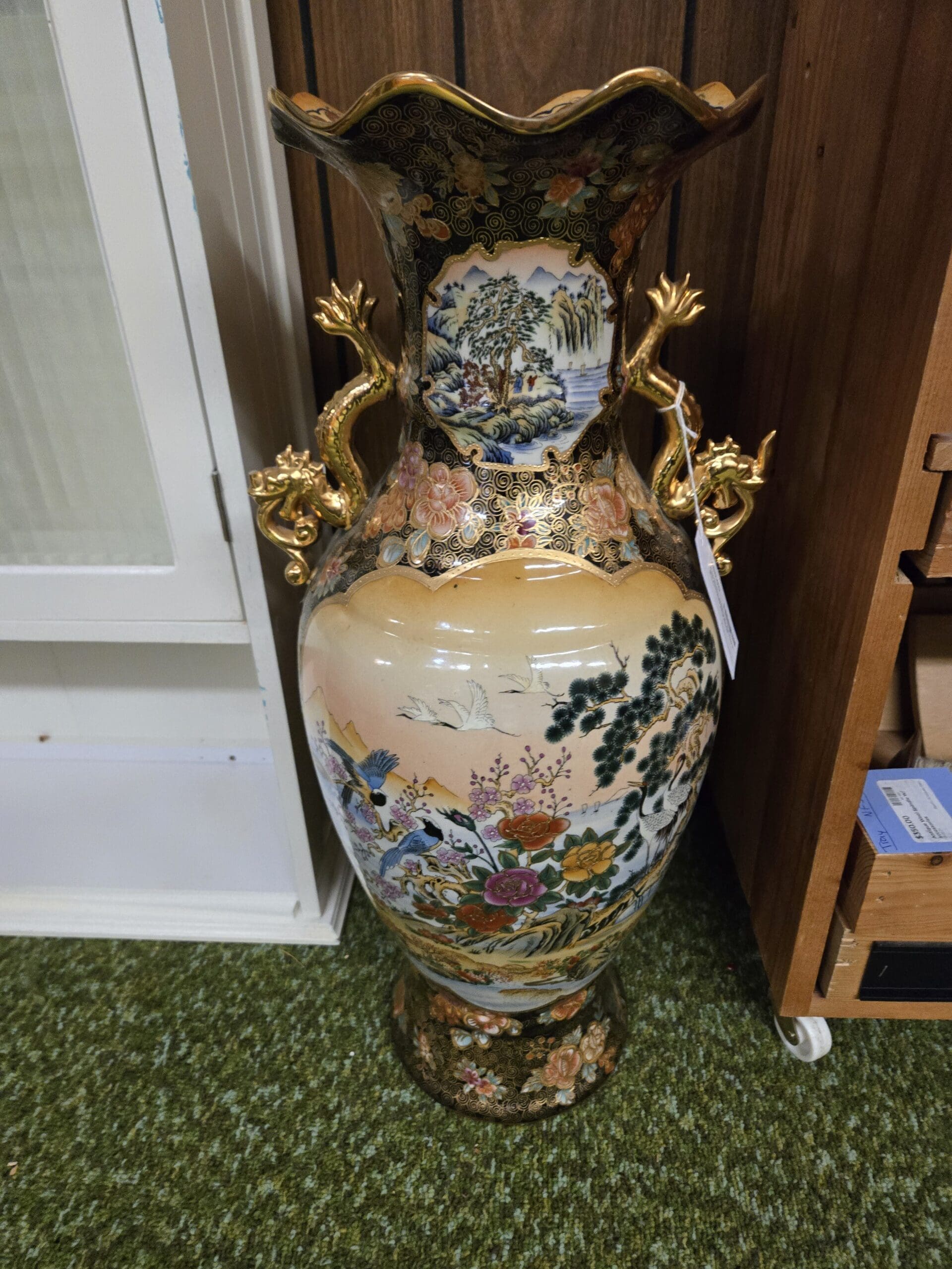 Hand-painted Japanese Satsuma-style floor vase, cream and peach ground decorated with cranes, peonies, chrysanthemums, and pine trees, with mountain landscape reserve panels and gold scrollwork on a black neck, fluted ruffled rim, gilded ceramic dragon-form handles, and a matching black and floral plinth base at Shop 24, Pacific Antiques Mall in Tacoma, WA.