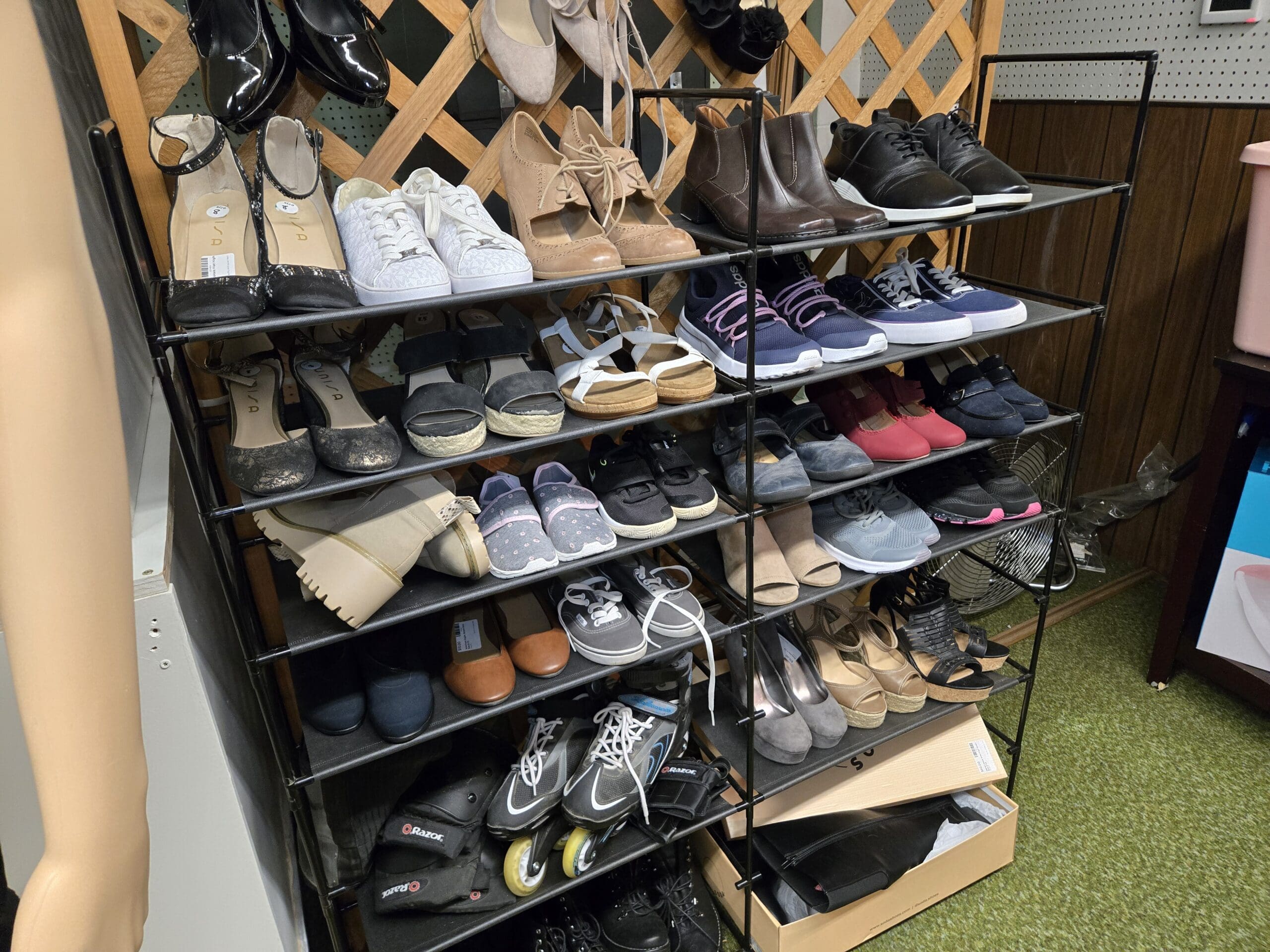 Multi-tier black wire shoe rack stocked with women's heeled sandals, white sneakers, tan ankle boots, brown leather boots, black sneakers, espadrille flats, cream lug-sole platform boots, gray slip-ons, navy athletic shoes, beige wedges, and a pair of Razor inline skates on the bottom shelf at Shop 92, Pacific Antiques Mall in Tacoma, WA.
