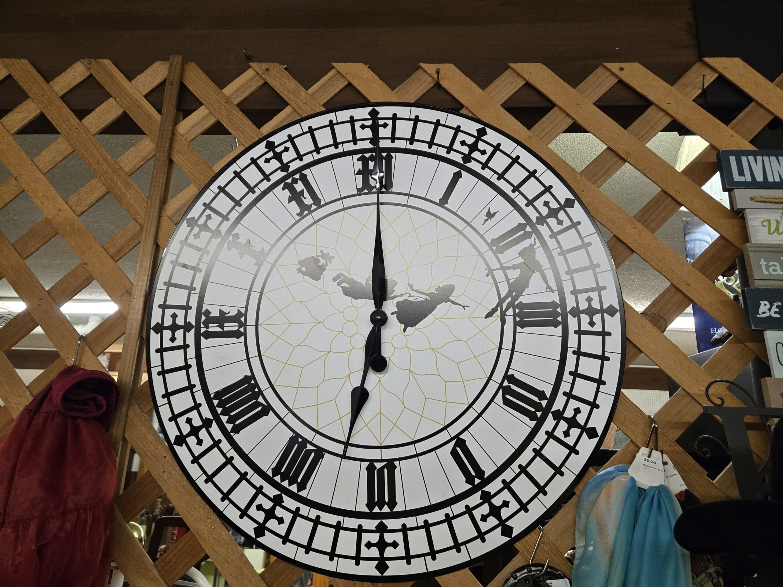 Large decorative Big Ben wall clock hung on a wood lattice wall, with a white face, Roman numerals in black Gothic lettering, cathedral cross details around the outer ring, silhouettes of Peter Pan, Wendy, John, and Michael flying across the center over a yellow filigree backing, and black hour and minute hands at Shop 75, Pacific Antiques Mall in Tacoma, WA.