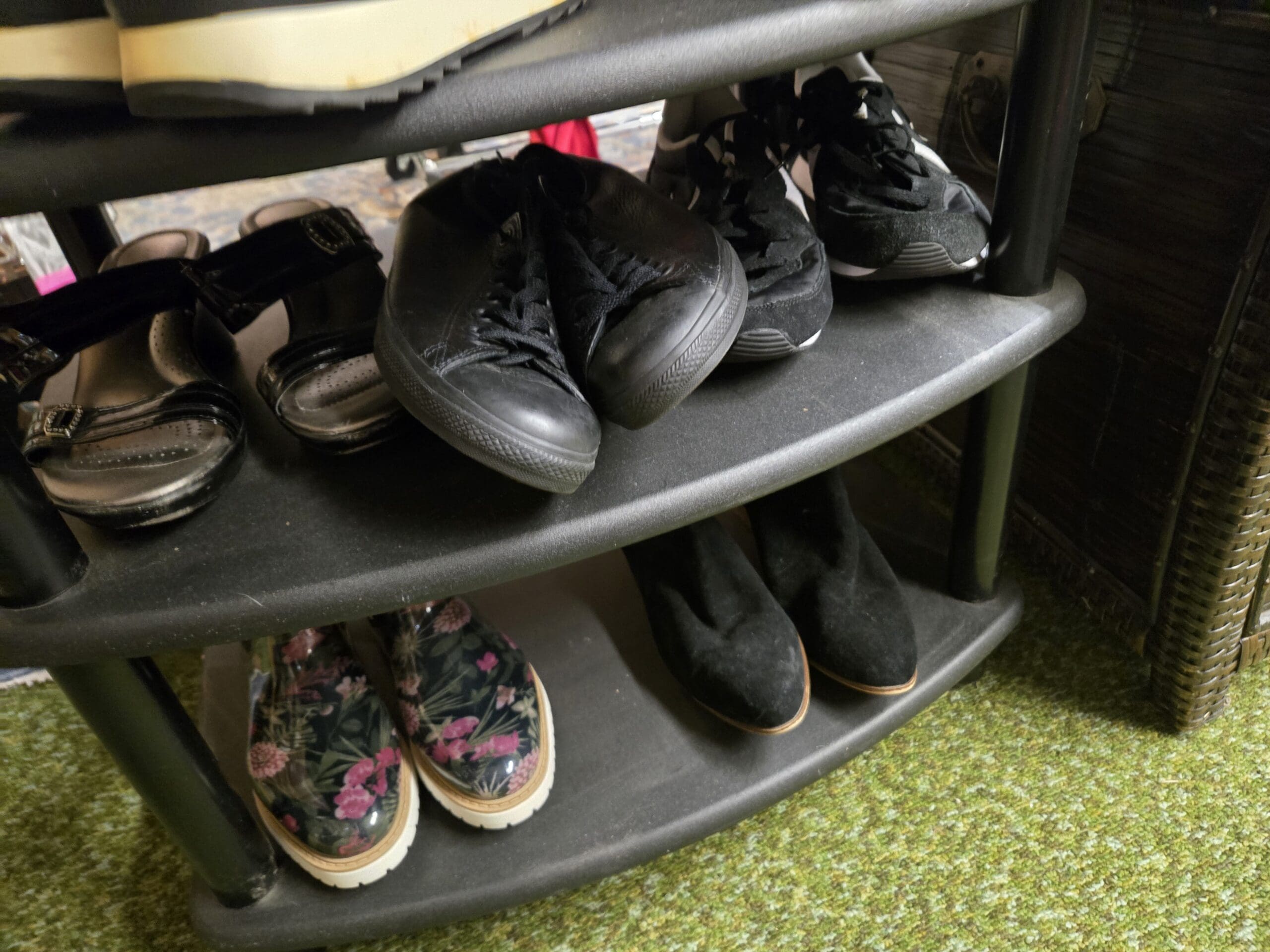 Lower shelves of the black shoe rack with black slingback sandals, low-top black canvas Converse Chuck Taylor sneakers, and black low-top athletic sneakers on the middle shelf, with floral-print pull-on rain boots in black with pink flowers and black suede ankle booties on the bottom shelf at Shop 75, Pacific Antiques Mall in Tacoma, WA.