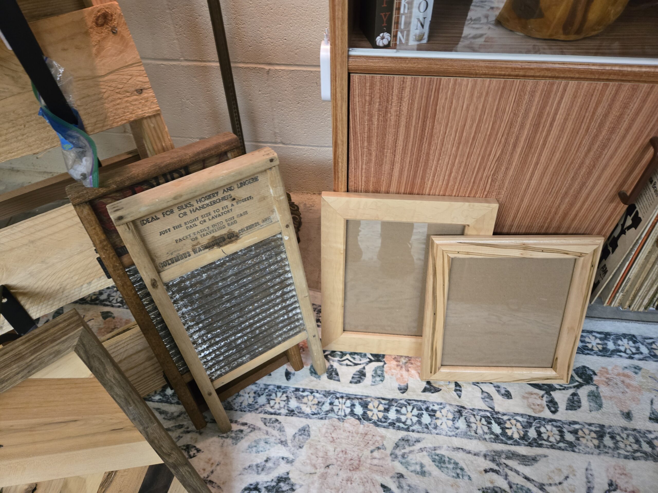 Columbus Washboard Co. lingerie washboard with a corrugated metal rubbing surface and wooden frame, printed for silks, hosiery, lingerie and handkerchiefs, a second wooden washboard behind it, and two light figured-wood picture frames, one with dark streaks in the grain, at Shop 73, Pacific Antiques Mall in Tacoma, WA.