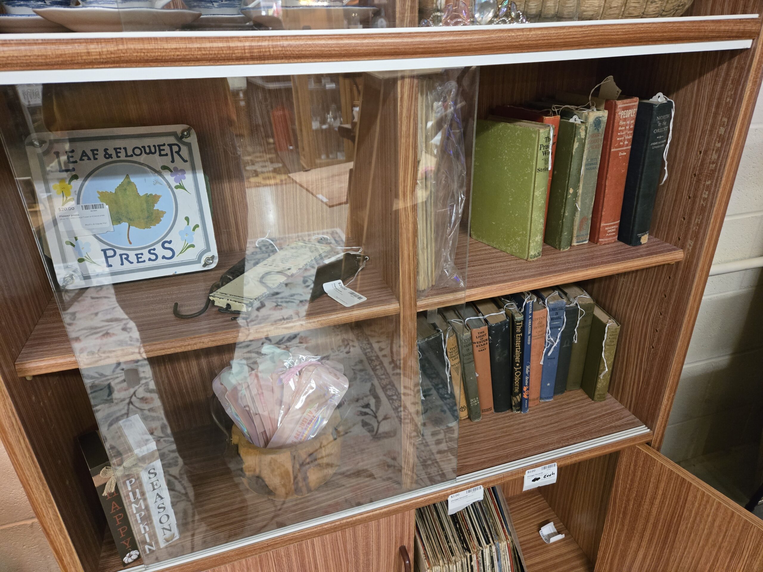 Leaf & Flower Press with a painted maple leaf and wildflowers, an antique hanging spring scale with a hook, a Happy Pumpkin Season block sign, a carved wooden bowl, and vintage cloth hardcover books including Zane Grey's The Light of Western Stars and Anne Morrow Lindbergh's North to the Orient, with vinyl records below, at Shop 73, Pacific Antiques Mall in Tacoma, WA.