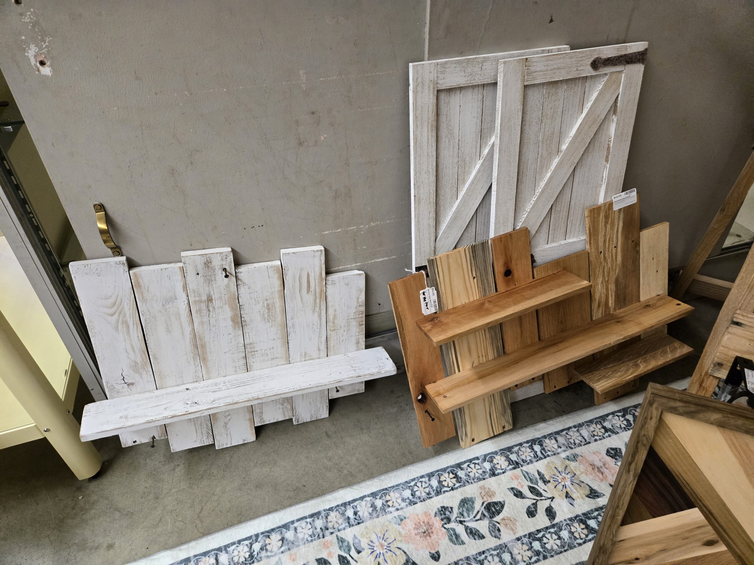 Whitewashed distressed plank wall shelf with a single ledge, a stepped reclaimed wood wall shelf in mixed pine and oak tones with three ledges, and a pair of white barn-door wall panels with Z-bracing and a dark strap hinge at Shop 73, Pacific Antiques Mall in Tacoma, WA.