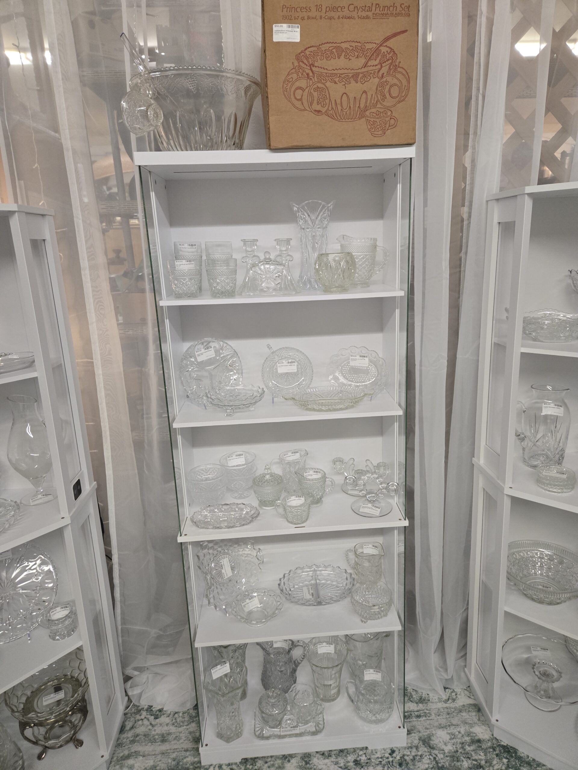 Indiana Glass Princess 18-piece crystal punch set box beside a grape-and-leaf punch bowl with ladle and cups, Anchor Hocking Wexford old fashioned glasses, tumblers and pitcher, a Prescut butter dish, double candlesticks, a fan-top vase, an Irena Poland crystal divided relish dish, a Stars and Bars nappy dish and creamer, a Denver Furniture Co. promotional oval tray, Dublin dessert bowls, a Wexford creamer and covered sugar, a Pineapple pitcher, Imperial Candlewick double candlesticks, a cube-pattern divided relish dish, a Star of David pitcher, and a Star of David sugar, creamer and tray set at Shop 20, Pacific Antiques Mall in Tacoma, WA.