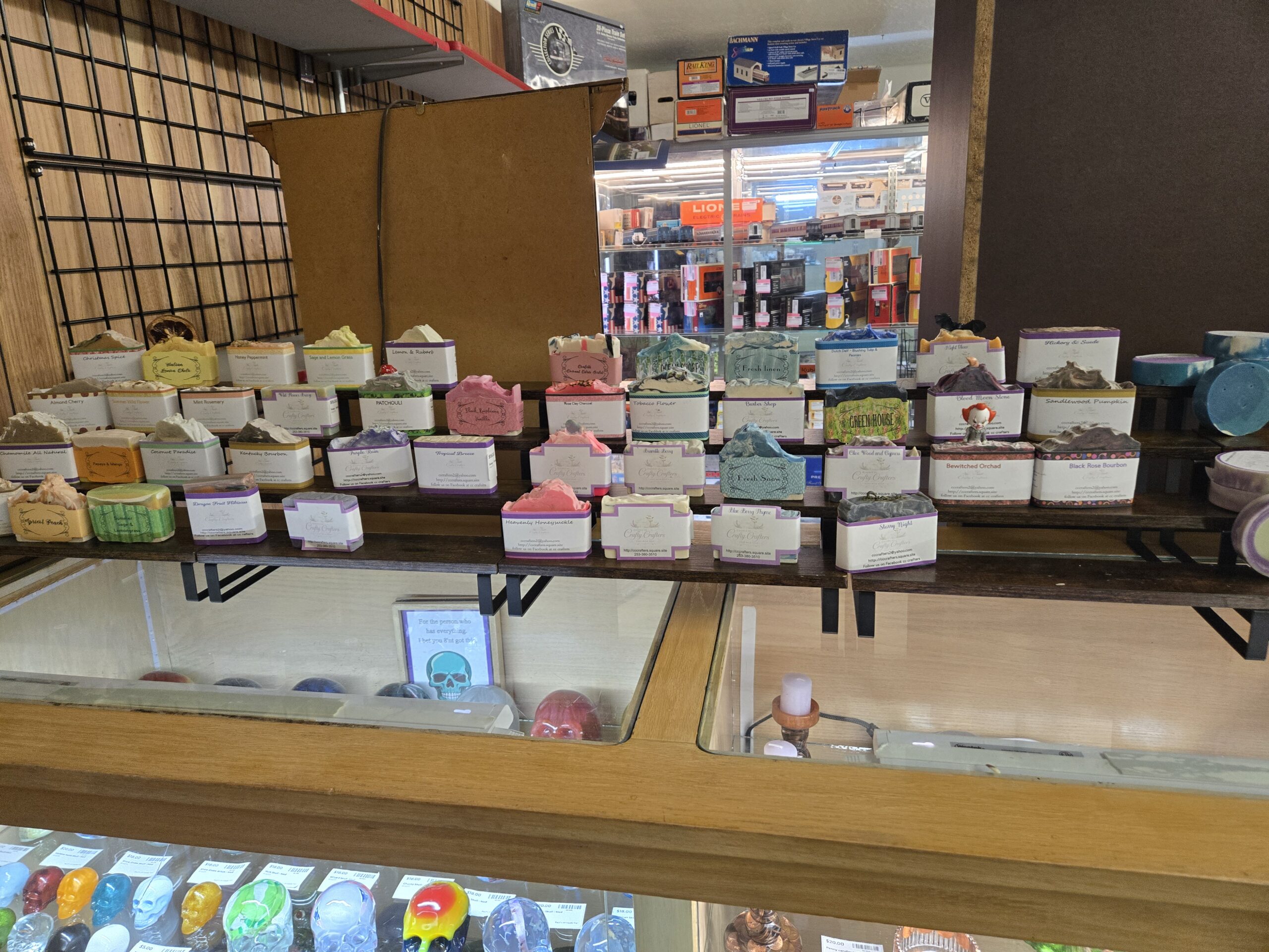 Rows of Crafty Crafters handmade bar soaps with swirled and frosted tops on tiered wooden risers, labeled Christmas Spice, Honey Peppermint, Sage and Lemon Grass, Almond Cherry, Mint Rosemary, Patchouli, Tobacco Flower, Barber Shop, Fresh Linen, Green House, Hickory & Suede, Kentucky Bourbon, Coconut Paradise, Papaya & Mango, Apricot Peach, Bramble Berry, Heavenly Honeysuckle, Starry Night, Bewitched Orchard and Black Rose Bourbon, with round soap pucks and a small Pennywise figure on one bar at Shop 333, Pacific Antiques Mall in Tacoma, WA.