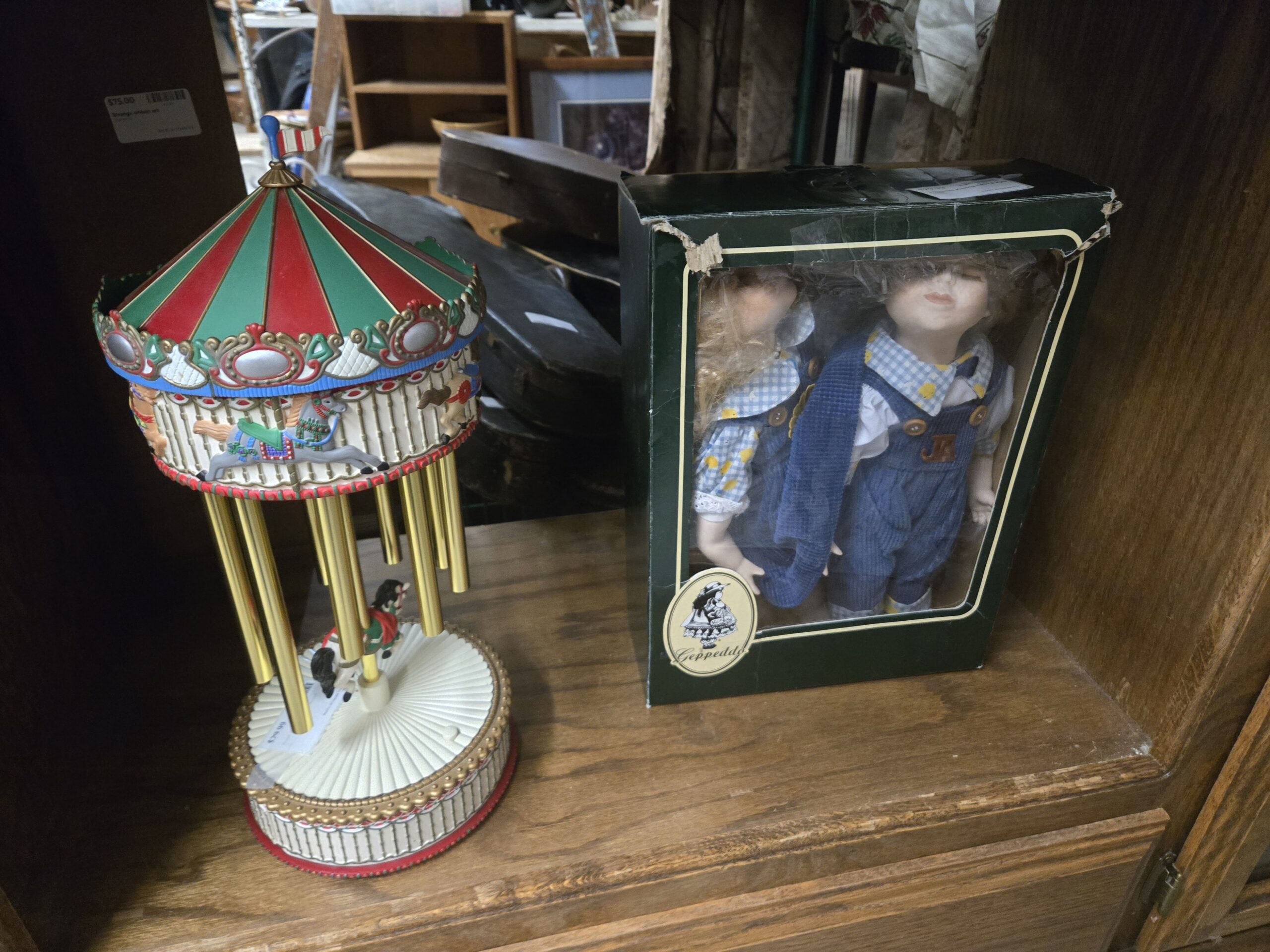 Carousel with a red and green striped canopy, painted carousel horses and gold chime tubes, and a boxed Geppeddo porcelain boy and girl doll pair in blue corduroy overalls and gingham shirts at Shop 54, Pacific Antiques Mall in Tacoma, WA.
