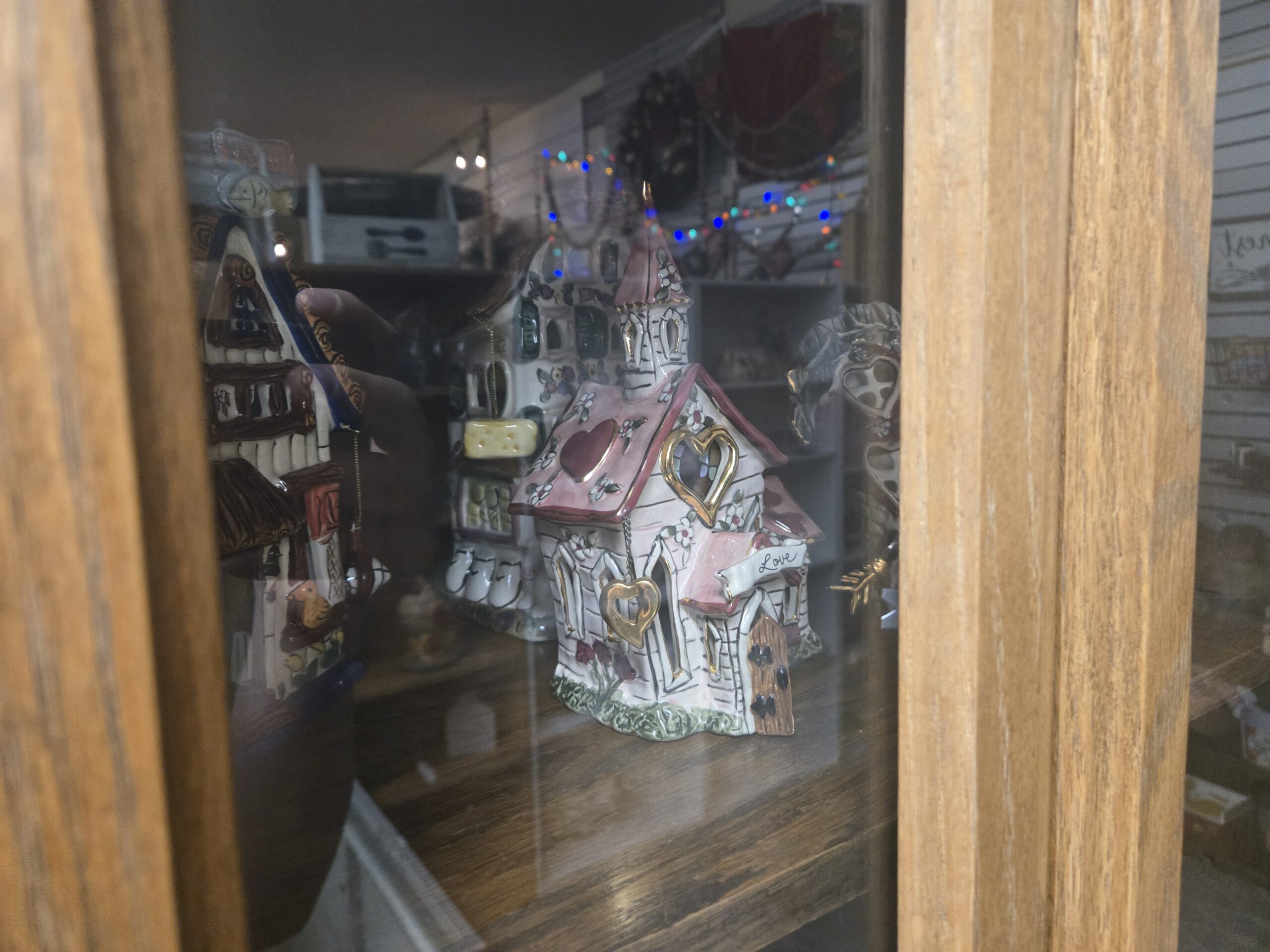 Hand-painted ceramic tealight houses, including a pink-roofed chapel with a steeple, gilt heart cutouts, a hanging gold heart and a “Love” banner, and a white floral house with a hanging cheese charm at Shop 54, Pacific Antiques Mall in Tacoma, WA.