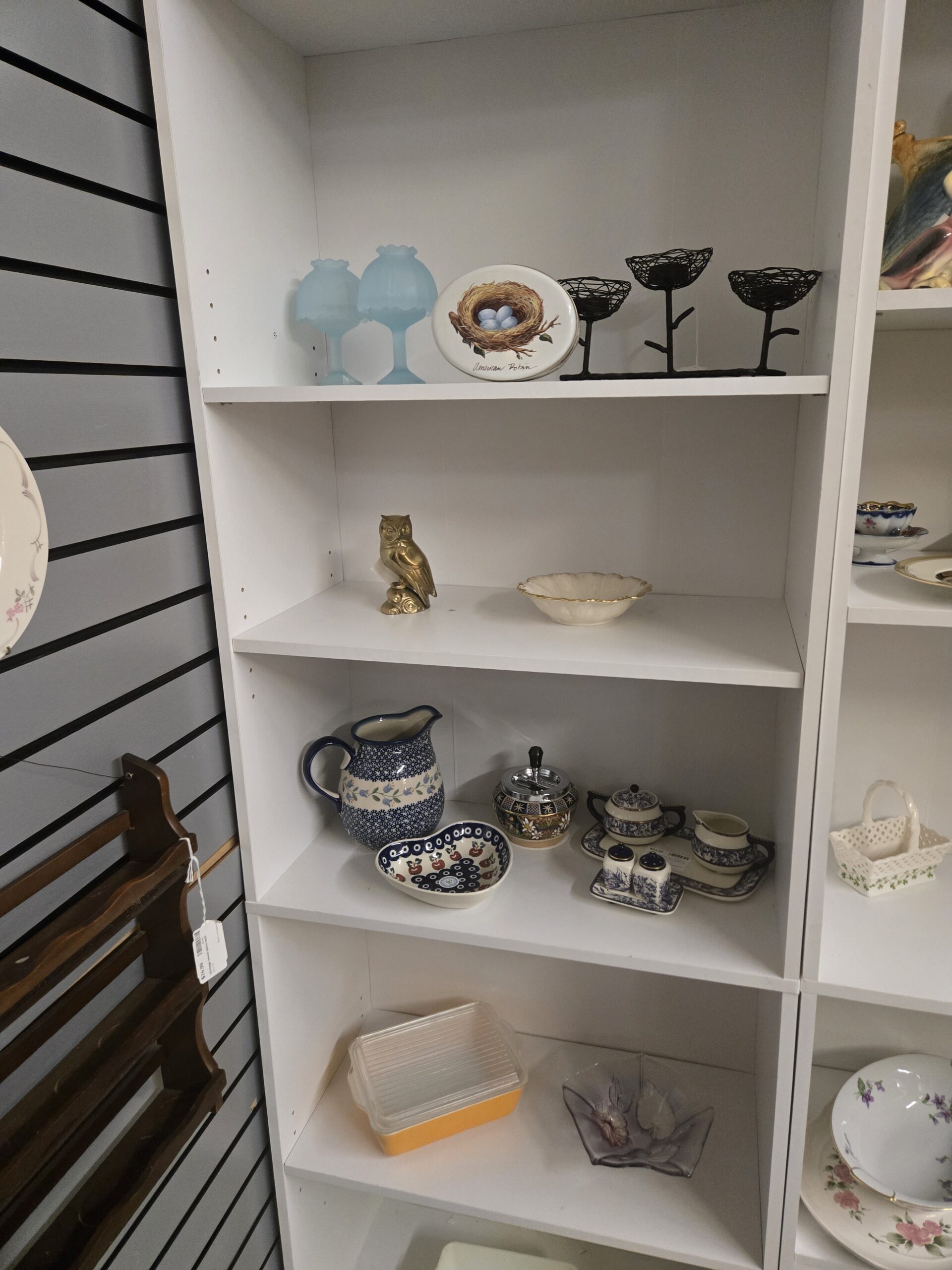 Pair of frosted blue satin glass fairy lamps, an American Robin nest plaque, a black wire nest tealight holder, a brass owl figurine, an ivory scalloped bowl with gold rim, a Polish pottery pitcher with blue florals and a peacock-eye heart dish with cherries, a push-button spinning ashtray with enamel floral decoration, a blue-and-white floral sugar bowl, creamer, tray and salt and pepper set, a yellow Pyrex refrigerator dish with ribbed glass lid, and a frosted lavender glass leaf dish at Shop 54, Pacific Antiques Mall in Tacoma, WA.