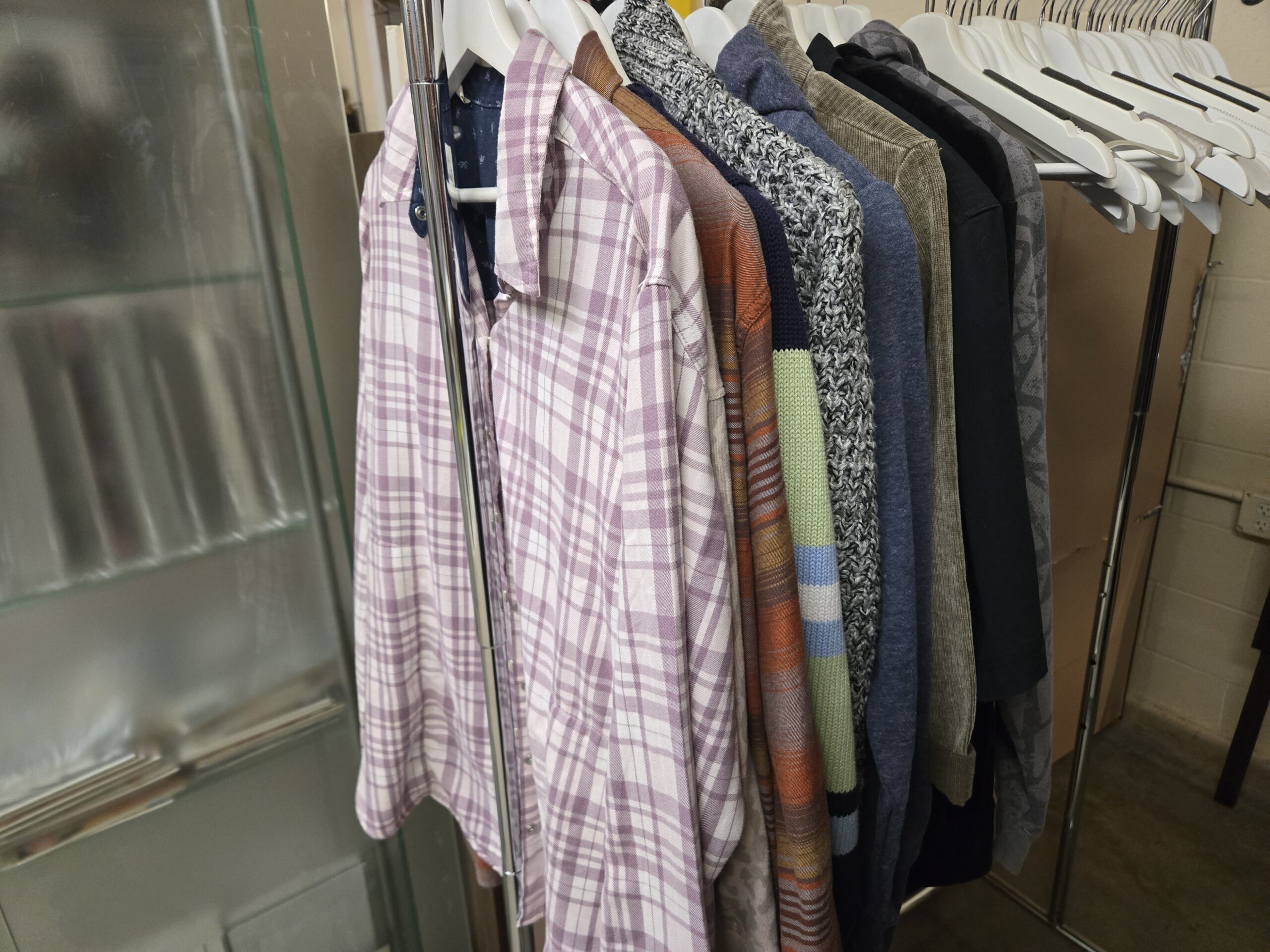 Lavender and white plaid shirt, a navy printed button-up shirt, a rust and orange striped shirt, a navy knit sweater with green, sky blue, and white striped sleeves, a marled black and white chunky knit sweater, a heather blue pullover, an olive corduroy shirt, a black jacket, and a gray printed pullover at Shop 89, Pacific Antiques Mall in Tacoma, WA.